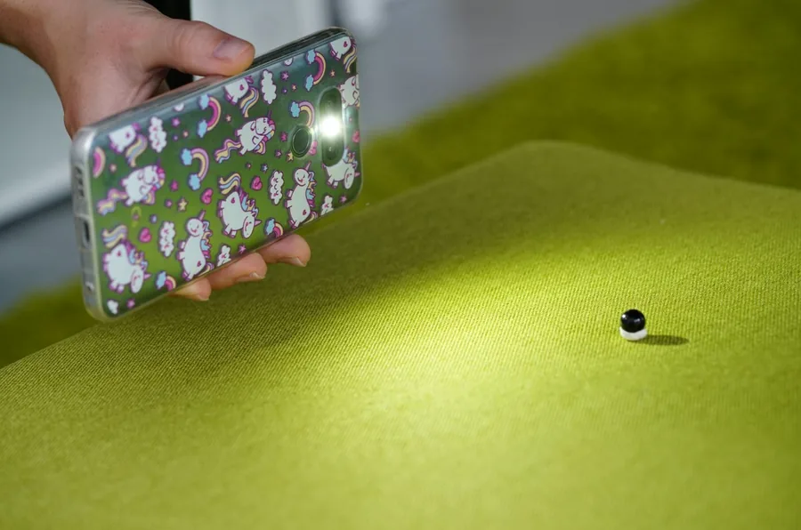 Hand moving a phone light above green fabric while the camera remains fixed